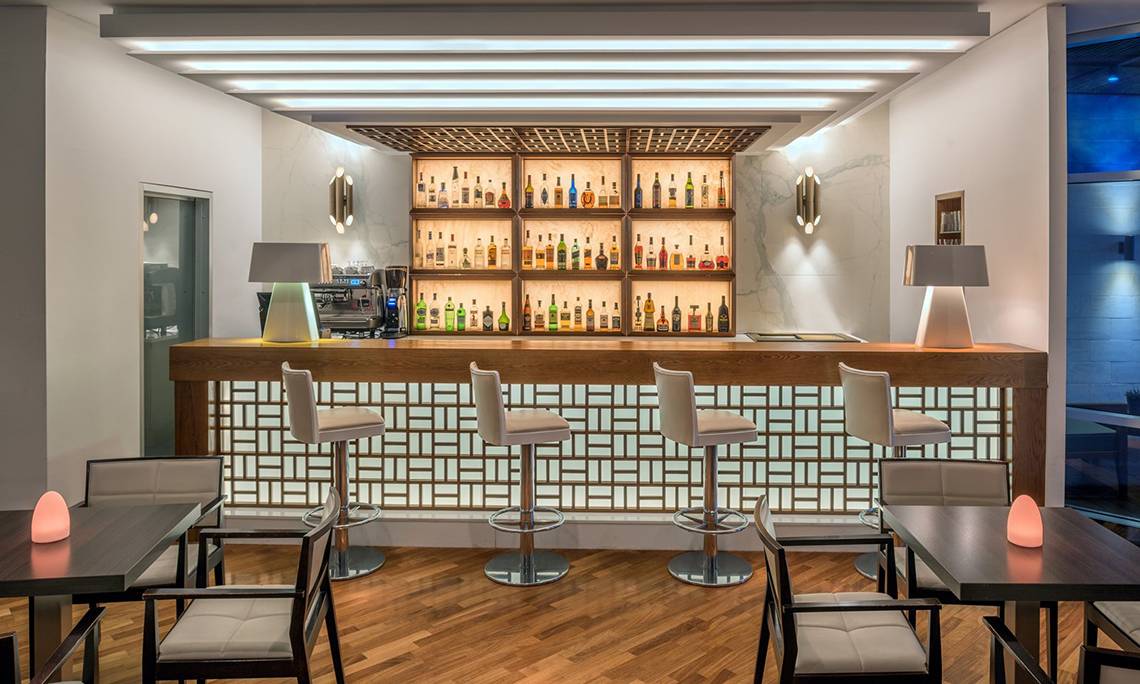 Innenansicht der Bar im Mediterranean Beach Hotel in Zypern mit einer Theke, mehreren Barhockern und einer Auswahl an Getränken.