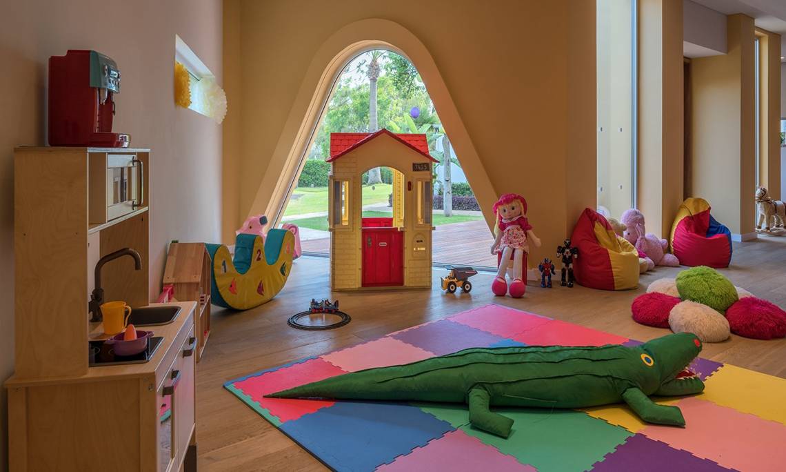Ein Kinderzimmer mit einer Spielmatte, Spielzeug, einem Haus, Puppen und einer Küche.