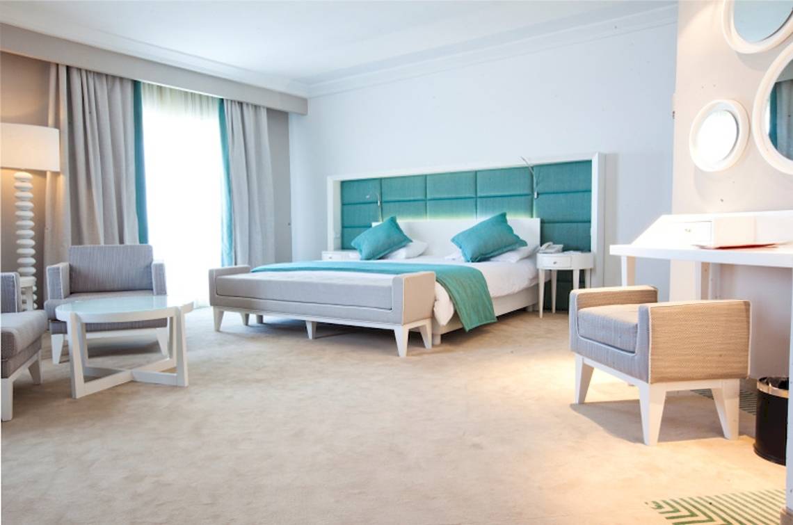 Schlafzimmer im El Mouradi Hammamet Hotel mit einem Bett, zwei Sesseln, einem Tisch und einer Lampe.