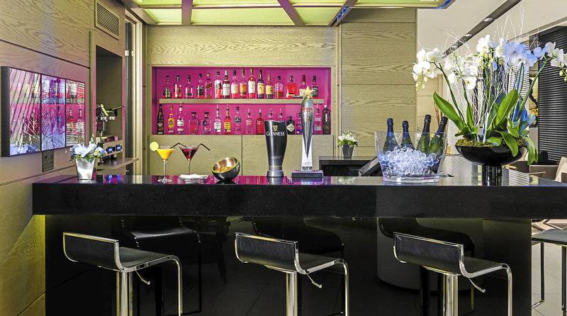 Innenansicht der Bar im H10 London Waterloo Hotel mit schwarzem Tresen, Cocktails, Trophäe, Pflanzen und Dekor.