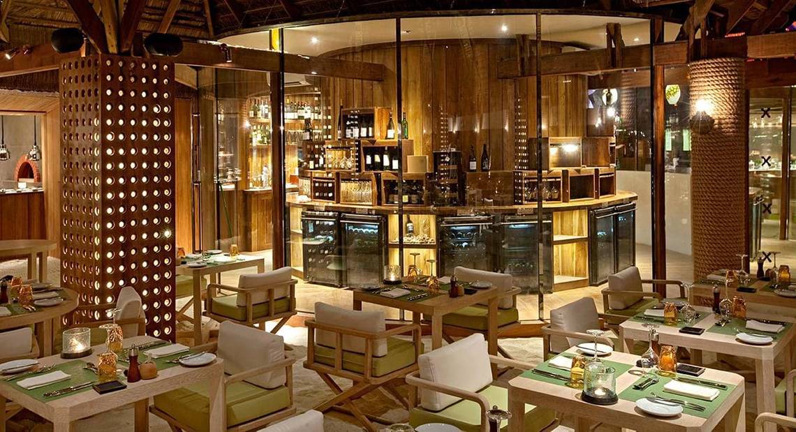 Innenansicht des Restaurants im Constance Moofushi Maldives, mit Tischen, Stühlen und Bar.