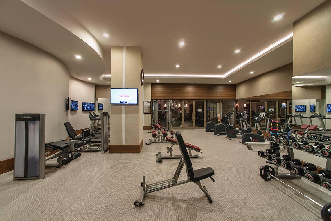 Fitness-Center im Aska Lara Resort & Spa mit verschiedenen Trainingsgeräten und Fernsehern an der Wand.
