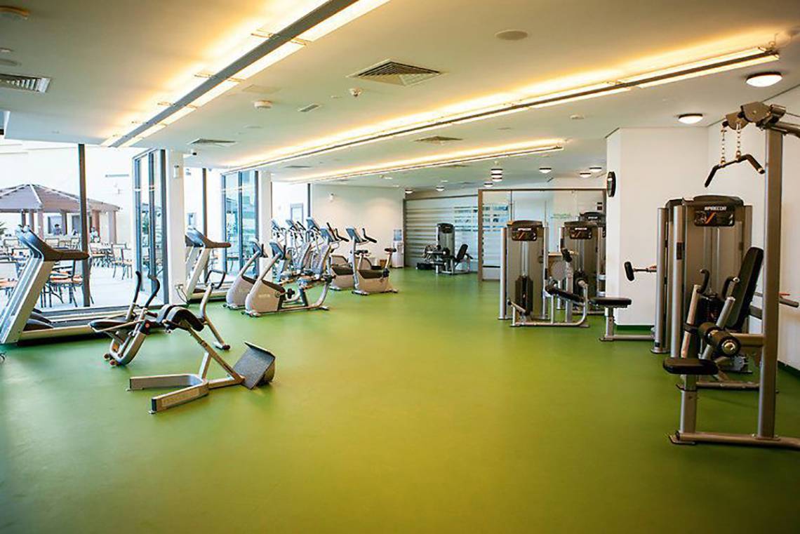 Fitnesscenter im JA Ocean View Hotel mit grünem Boden und vielen Trainingsgeräten.