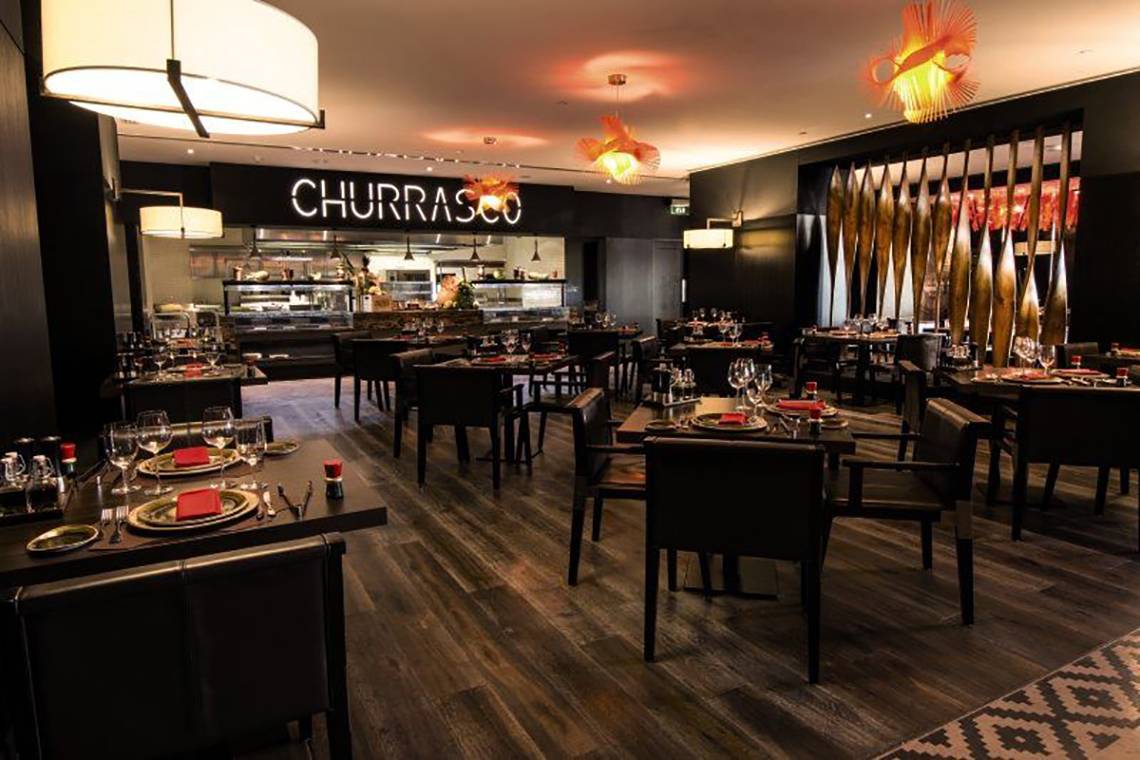 Innenbereich des Churrasco Restaurants im JA Ocean View Hotel mit gedeckten Tischen und Stühlen.
