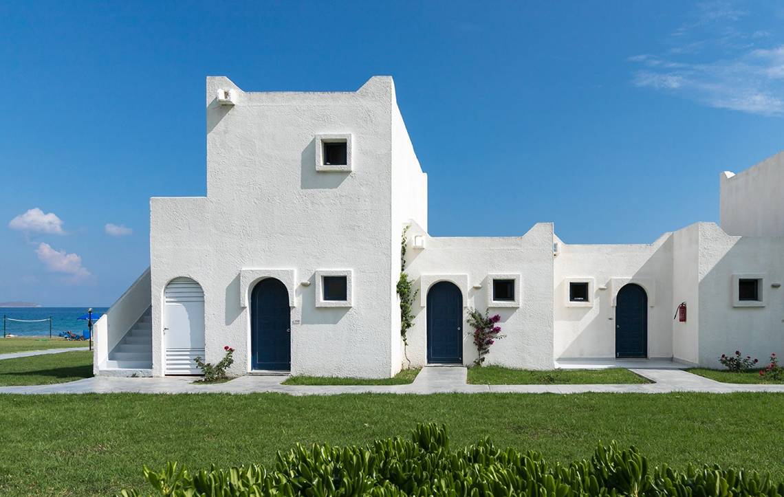 Außenansicht des Aeolos Beach Hotel auf Kos mit weißen Gebäuden, blauen Türen und grünem Rasen.