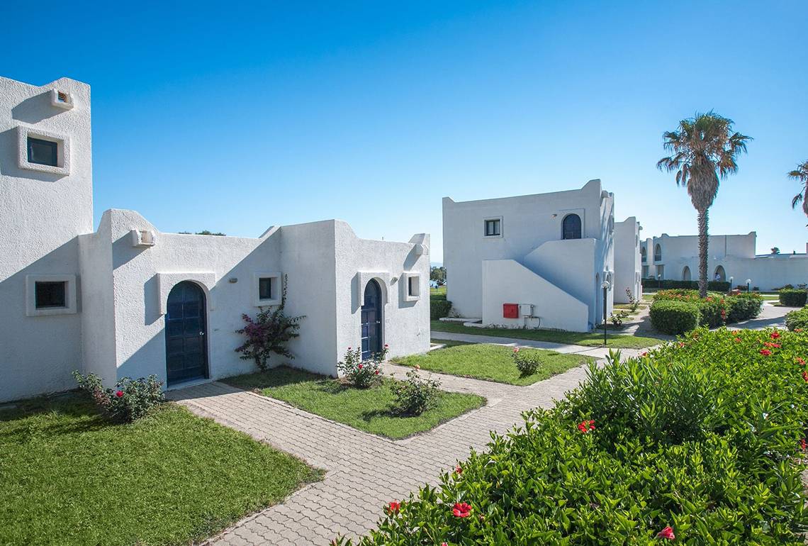 Außenansicht des Aeolos Beach Hotel in Kos mit weißen Gebäuden und gepflegtem Garten.