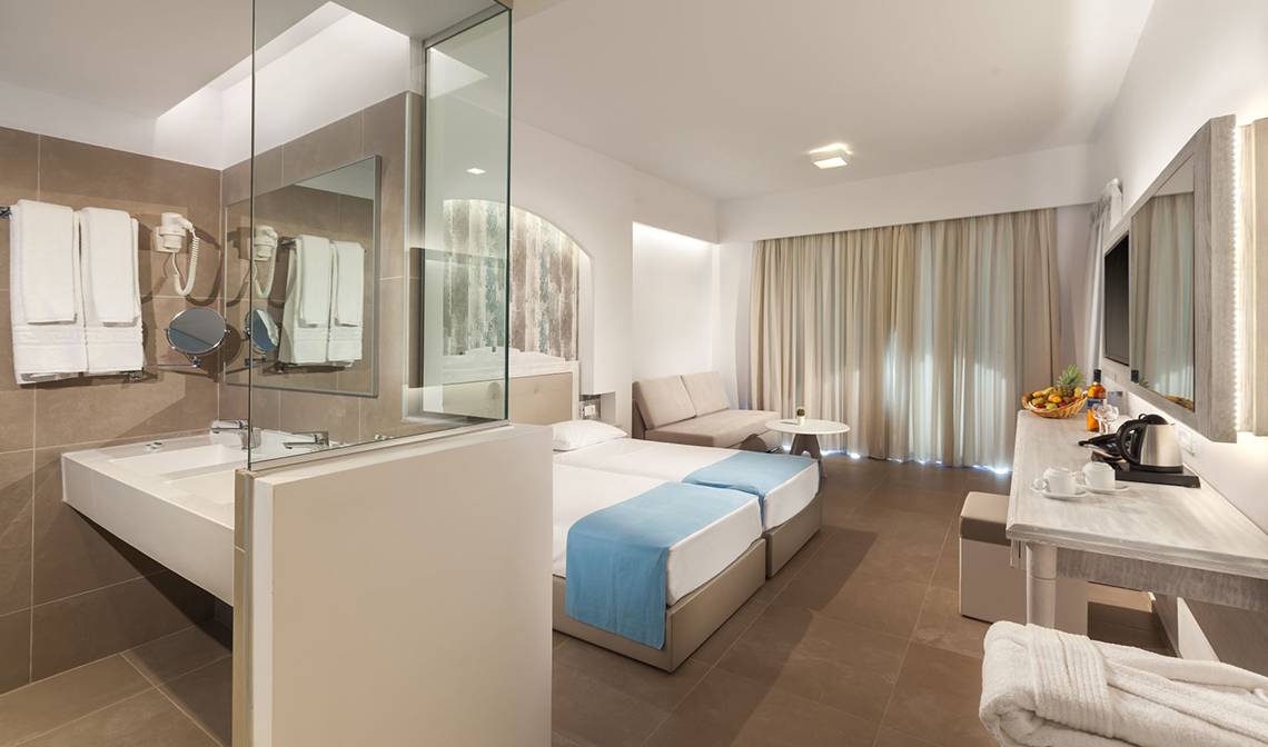 Hotelzimmer im Aeolos Beach Hotel auf Kos mit zwei Betten, Badezimmer und Sitzbereich.