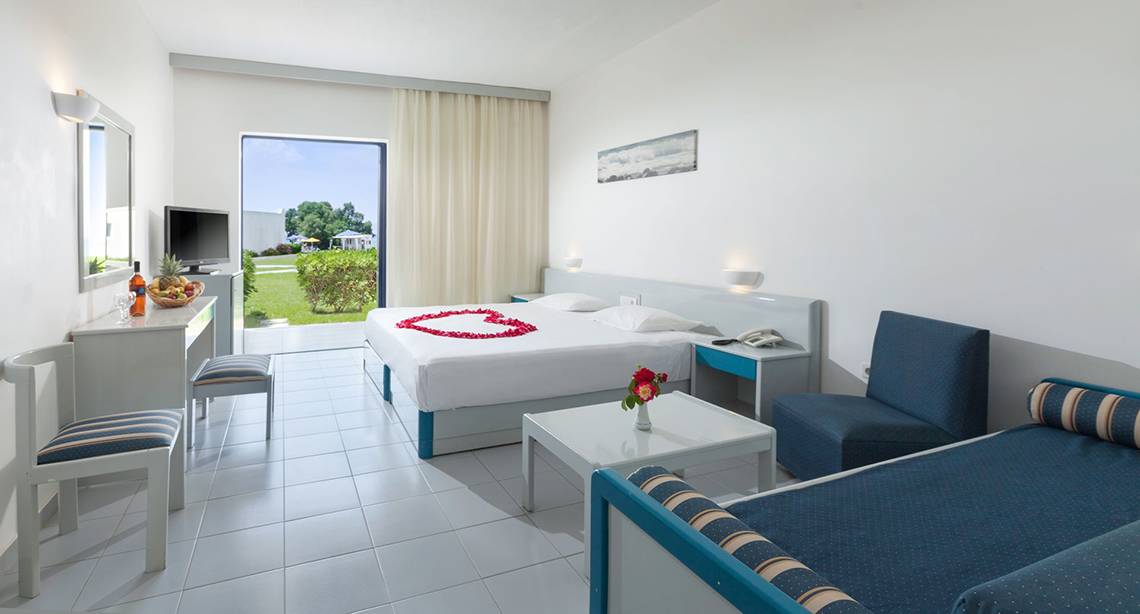 Zimmer im Aeolos Beach Hotel mit Herz-Dekoration auf dem Bett und Blick auf den Garten.