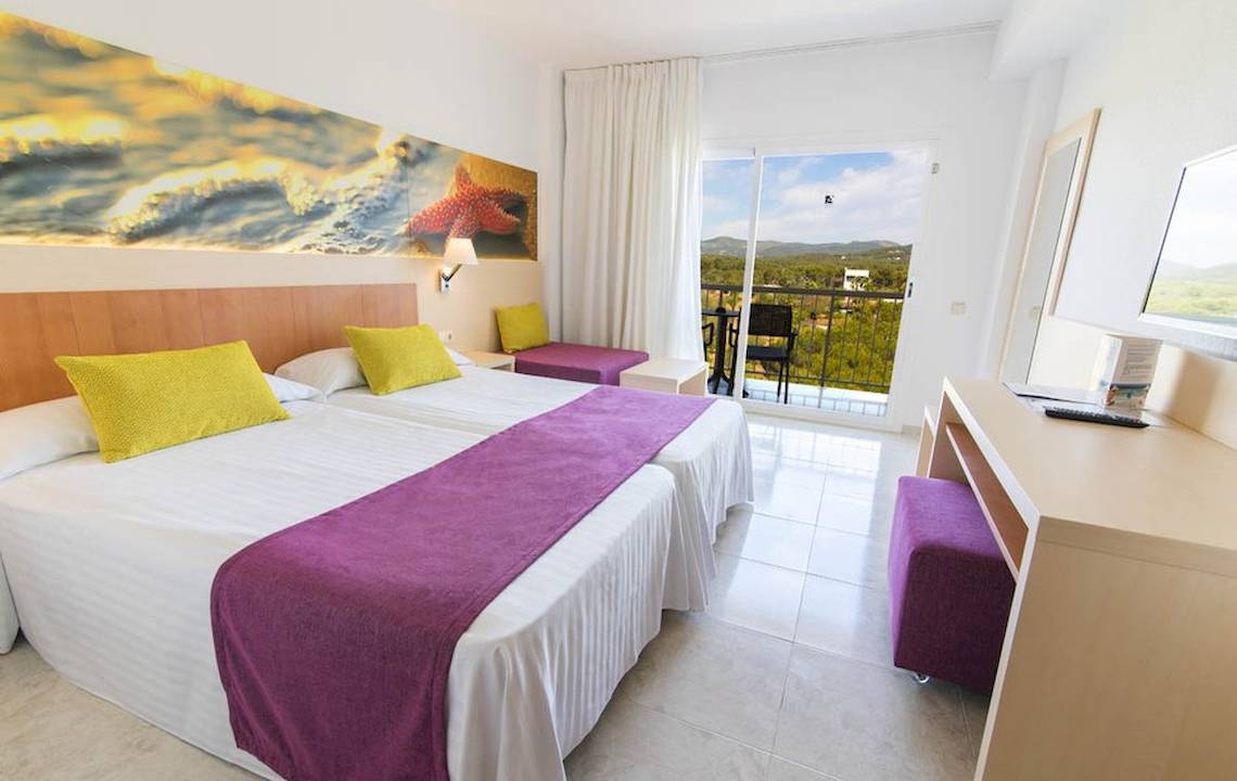 Helles Hotelzimmer im Moon Dreams Coral Beach mit zwei Betten, farbenfrohen Kissen und Blick auf die Landschaft.