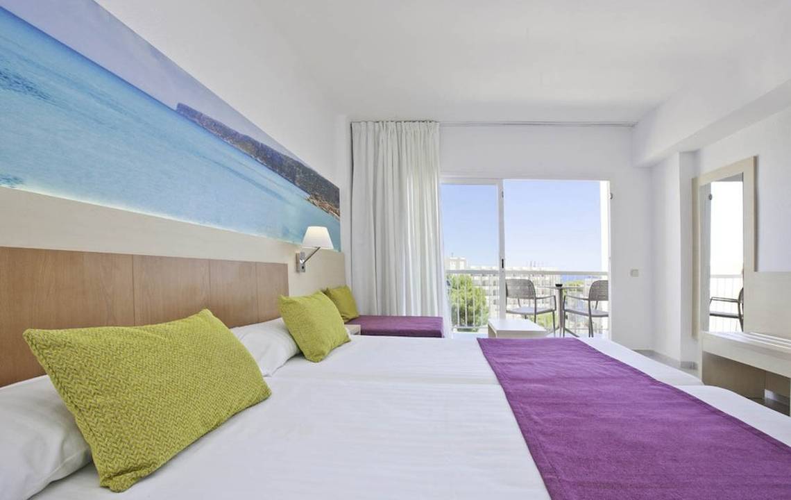 Ein helles Hotelzimmer im Moon Dreams Coral Beach mit zwei Betten und Blick auf das Meer durch große Fenster.