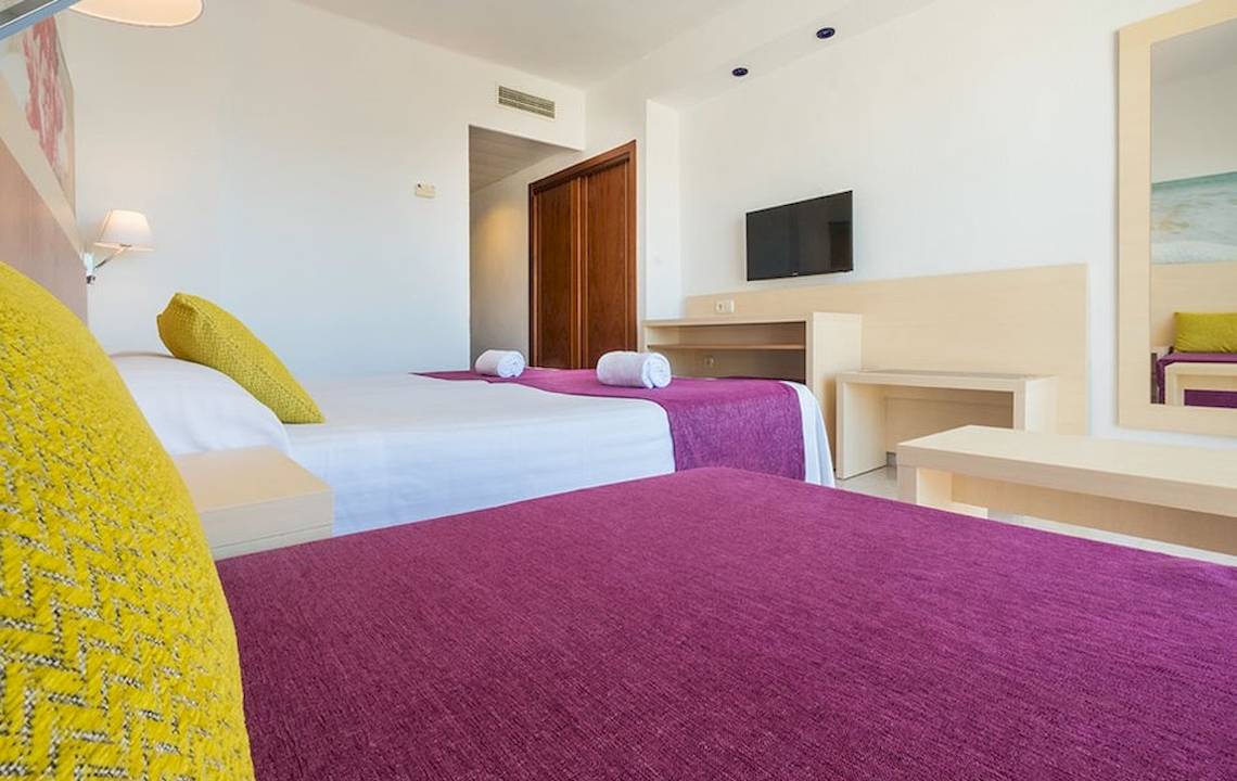 Gemütliches Zimmer im Moon Dreams Coral Beach mit zwei Betten, Fernseher und minimalistischer Einrichtung.