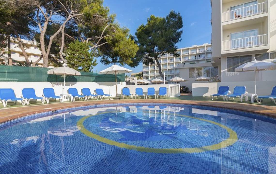 Poolbereich im Hotel Moon Dreams Coral Beach mit Liegen und Sonnenschirmen, umgeben von Bäumen und einem klaren Himmel.