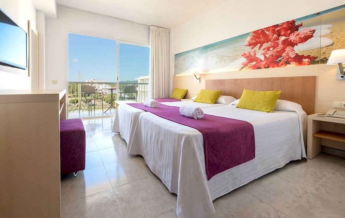 Helles Hotelzimmer im Moon Dreams Coral Beach mit zwei Betten, bunten Kissen und Blick auf die Terrasse.