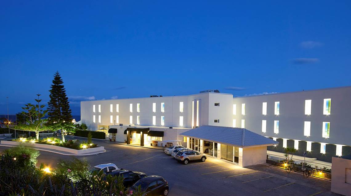 Außenansicht des Dimitra Beach Hotel & Suites bei Nacht mit beleuchteten Gebäuden und Autos im Parkbereich.