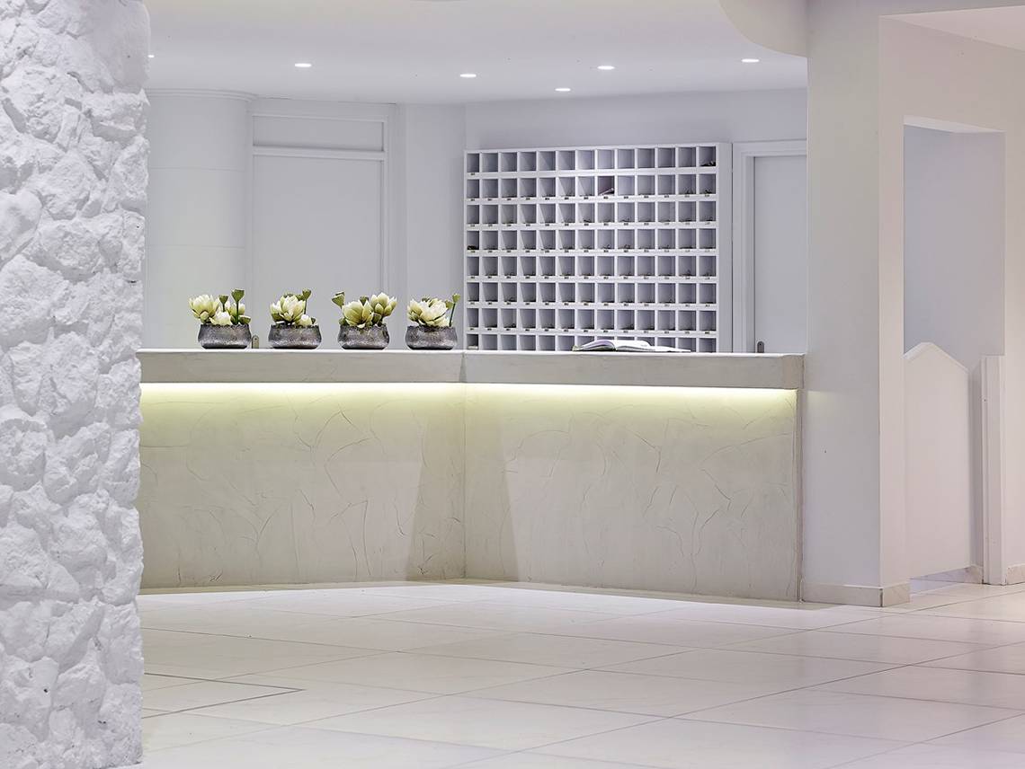 Rezeption des Dimitra Beach Hotel & Suites mit weißen Möbeln und vier Blumenvasen.