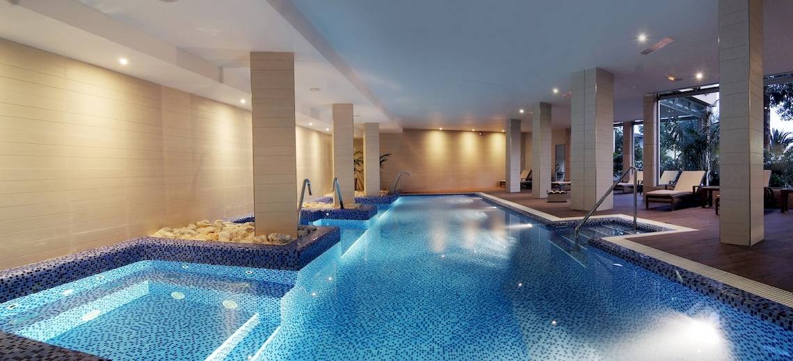 Innenpool des Zafiro Tropic Hotel mit blauem Wasser und weißen Wänden.