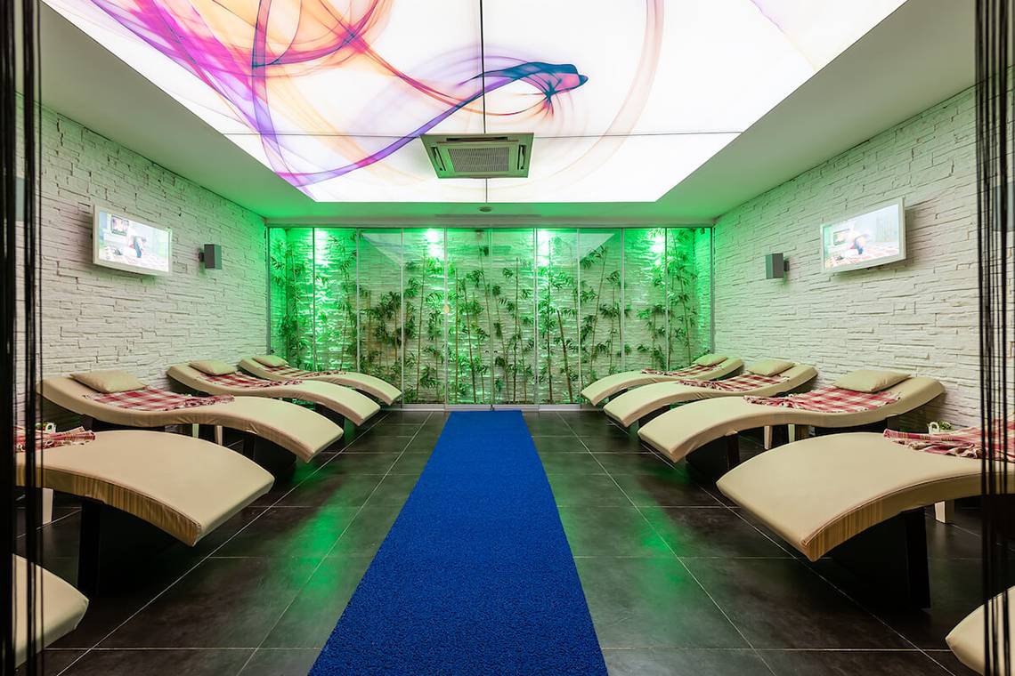 Loungebereich im White City Resort mit weißen Wänden, grünen Pflanzen und einer blauen Teppichbahn.