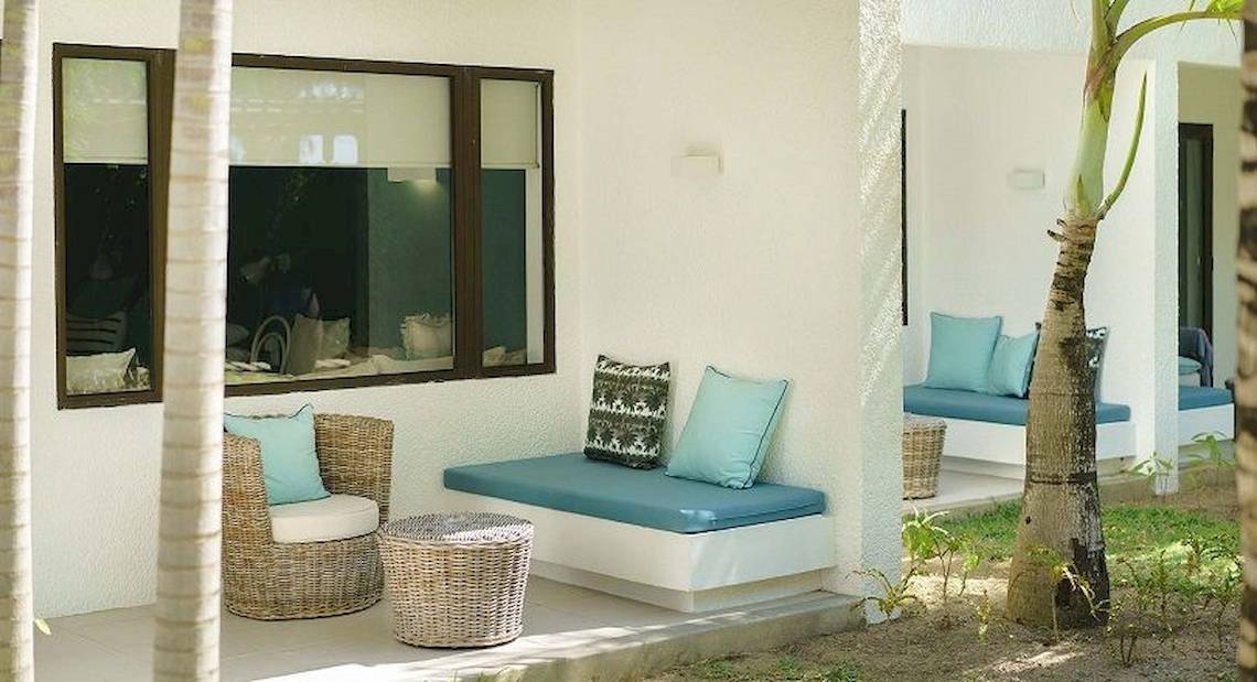 Loungebereich des Ravenala Attitude Hotels mit weißen Wänden, blauen Kissen und Korbmöbeln vor einem Fenster.
