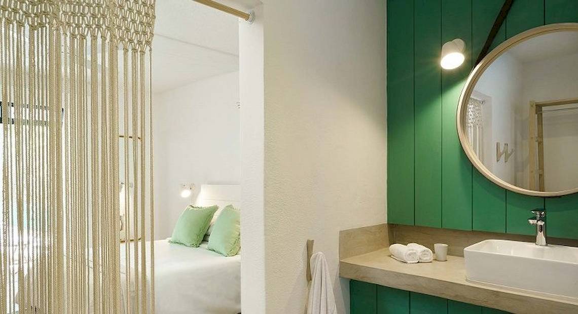 Innenansicht eines Zimmers im The Ravenala Attitude Hotel mit grünen Wänden, einem Bett, einem Spiegel und einem Waschbecken.