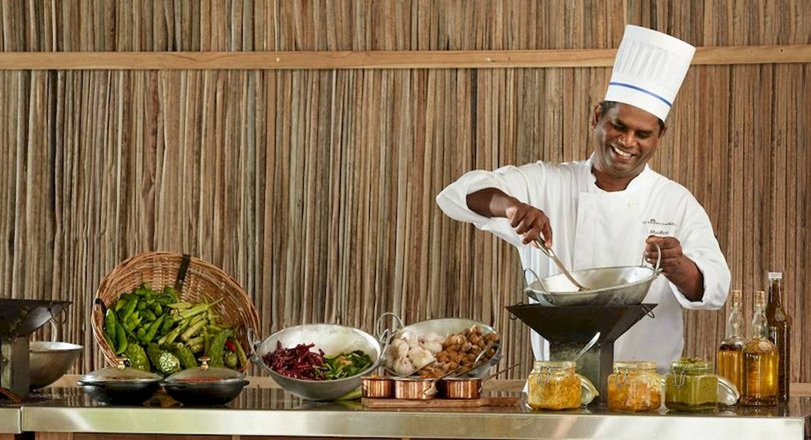 Ein Koch bereitet eine Mahlzeit im The Ravenala Attitude Hotel zu, umgeben von Zutaten und Küchenutensilien.