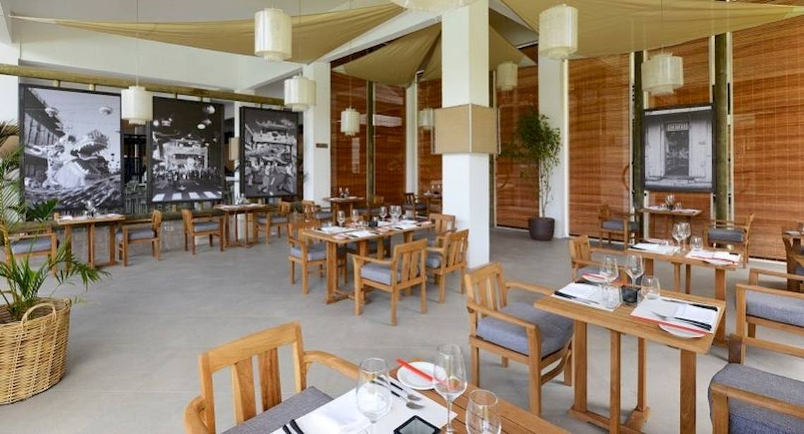 Innenansicht des Restaurants des Ravenala Attitude Hotels mit Holztischen, Stühlen und Dekoration.