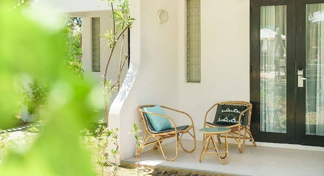 Der Vorgarten des Ravenala Attitude Hotels mit zwei Rattan-Stuhl, einem kleinen Tisch und einem schwarzen Eingangstor.