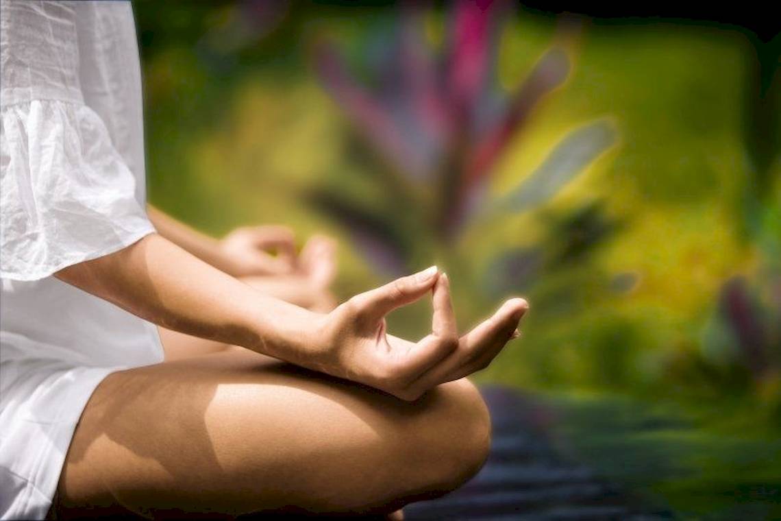 Frau sitzt im Garten und macht Meditation mit geschlossenen Augen