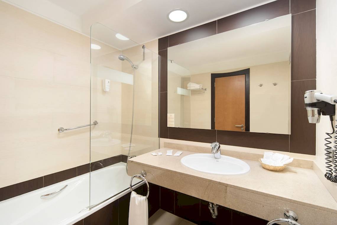 Ein Badezimmer im Lanzarote Village Hotel mit Badewanne, Spiegel und Föhn.