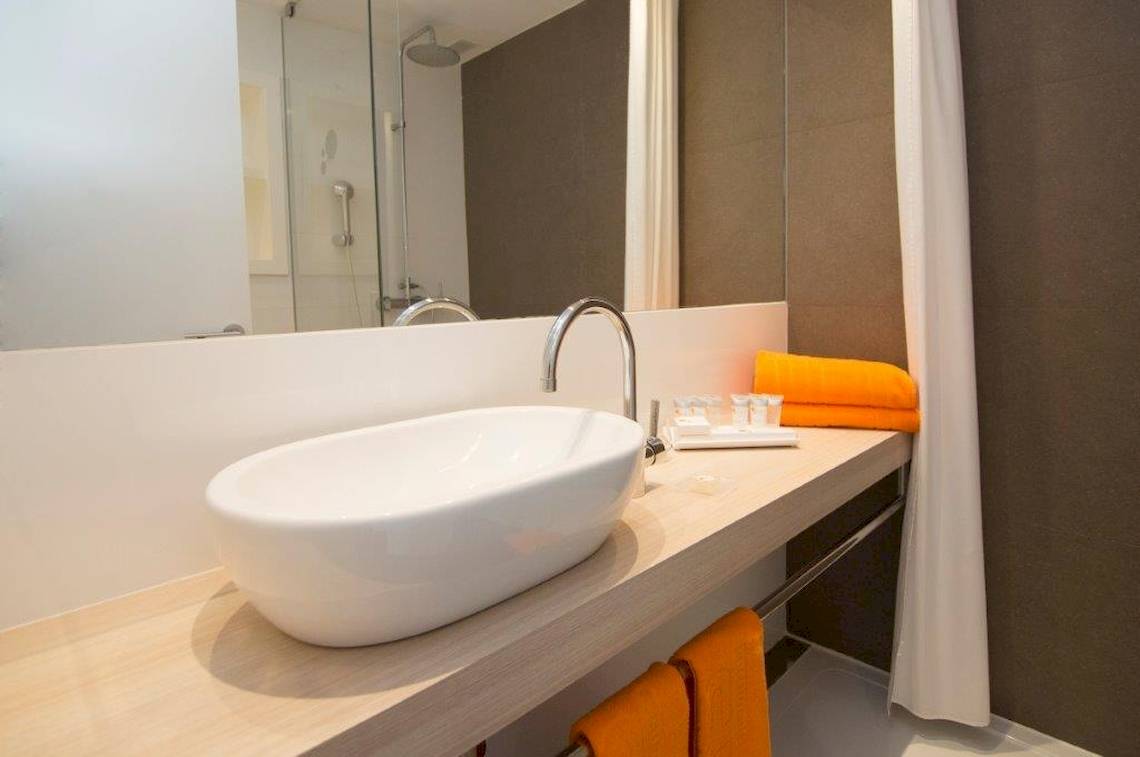 Badezimmer mit weißem Waschbecken, Spiegel und orange Handtüchern bei Ibiza Sun Apartments