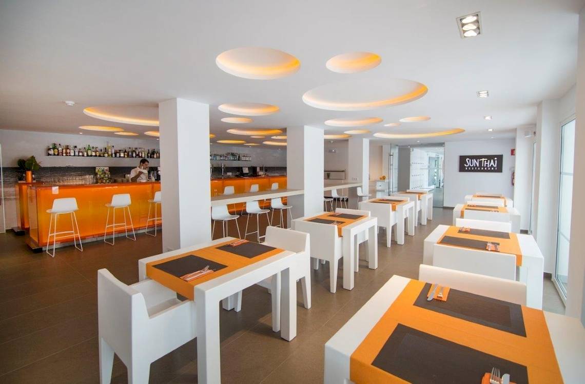 Innenansicht eines Restaurants mit orangenen Stühlen und runden Leuchten an der Decke, servierbar vorbereitete Tische.