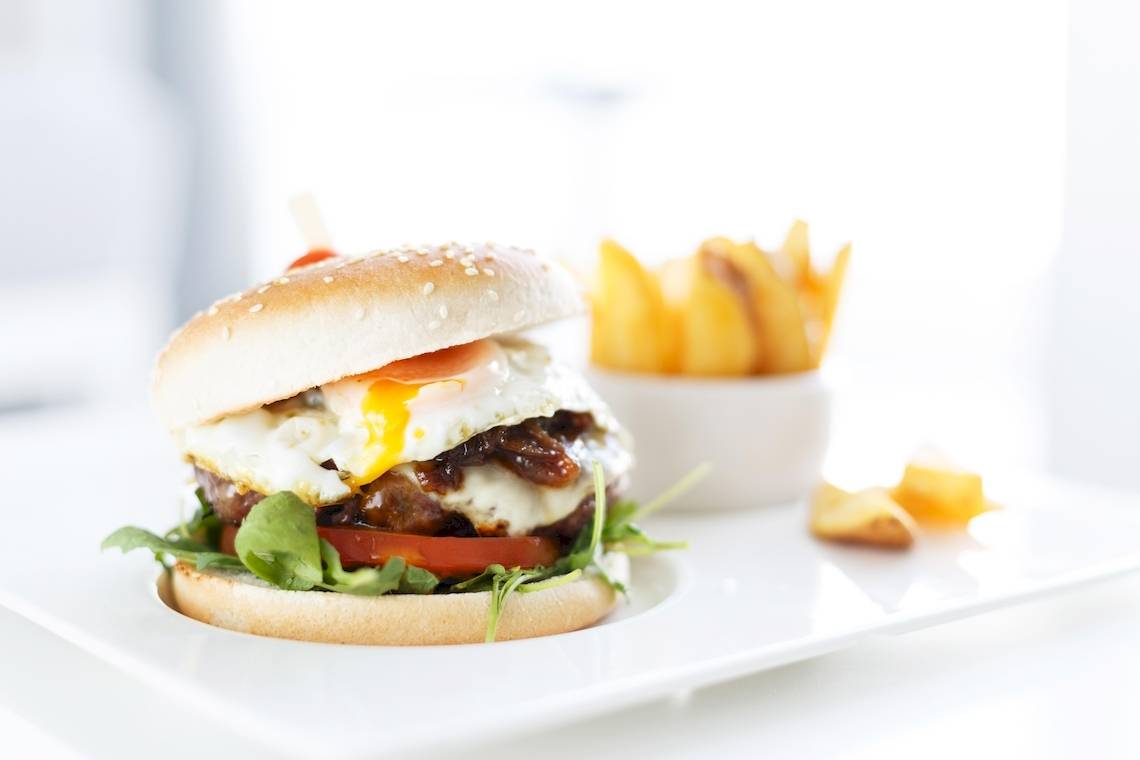 Ein Burger mit Ei auf einem weißen Teller mit Pommes