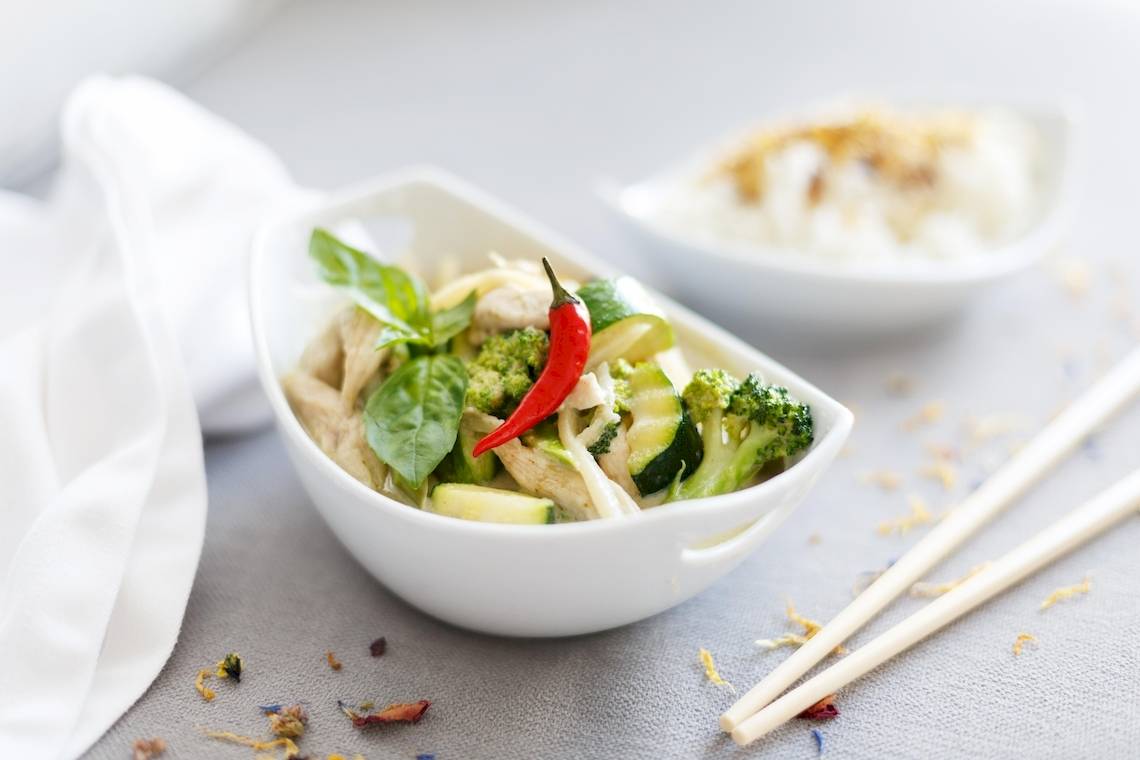 Asiatisches Gemüsegericht mit Hähnchen in weißen Schalen, serviert mit Reis und Essstäbchen.