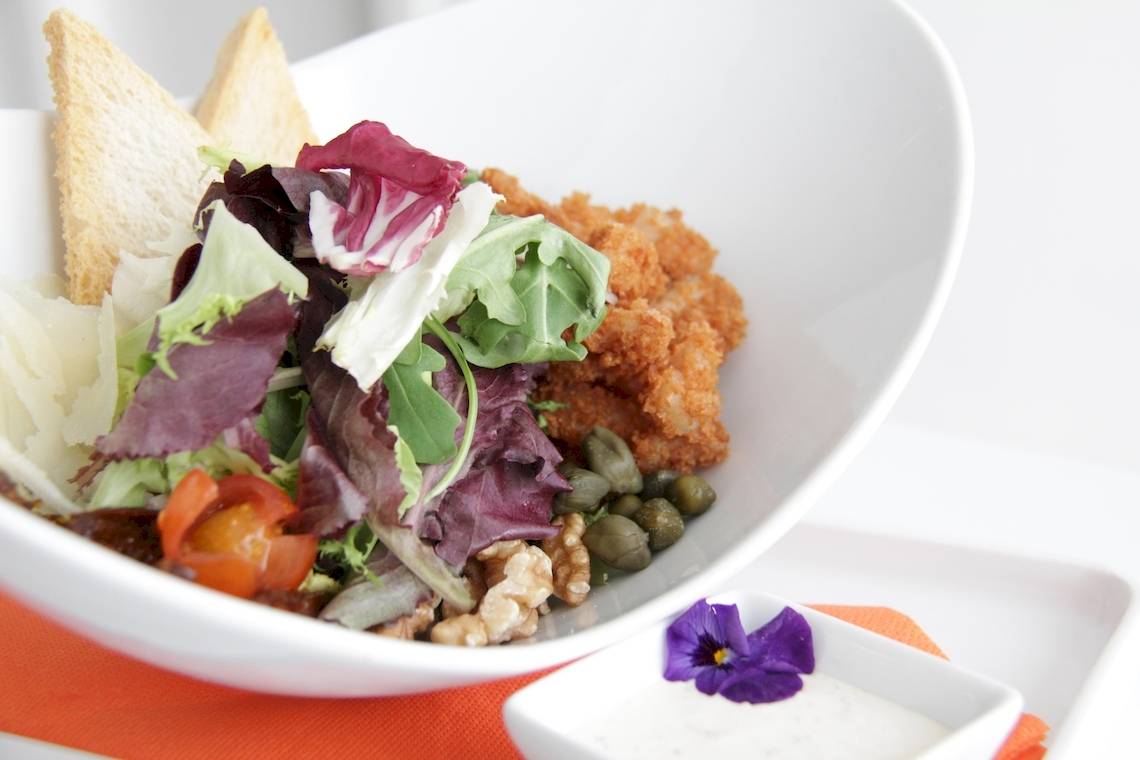Ein weißer Teller mit gemischtem Salat, Croutons, Walnüssen und einer kleinen Beilage.