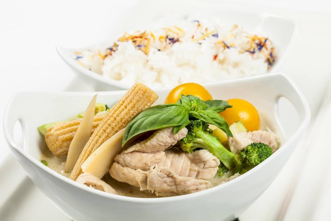 Gewürztes Huhn-Curry mit Reis und Gemüse in weißen Schüsseln auf weißem Hintergrund