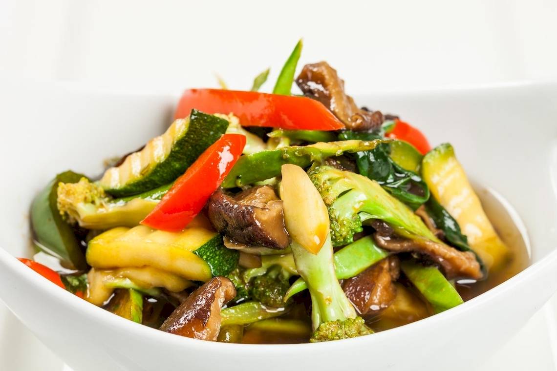 Ein weißer Teller mit asiatischem Gemüse, einschließlich Paprika, Zucchini und Brokkoli.