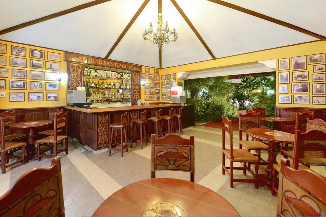 Bar Santiago im Iberostar Playa Alameda Hotel mit gelben Wänden, Holztischen und Stühlen, einer Theke und alten Fotos an der Wand.