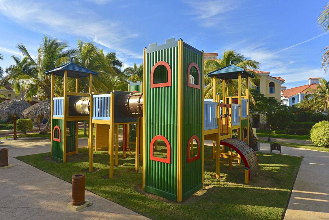 Kinderspielplatz im Iberostar Playa Alameda Hotel mit bunten Spielgeräten und Gebäuden im Hintergrund.