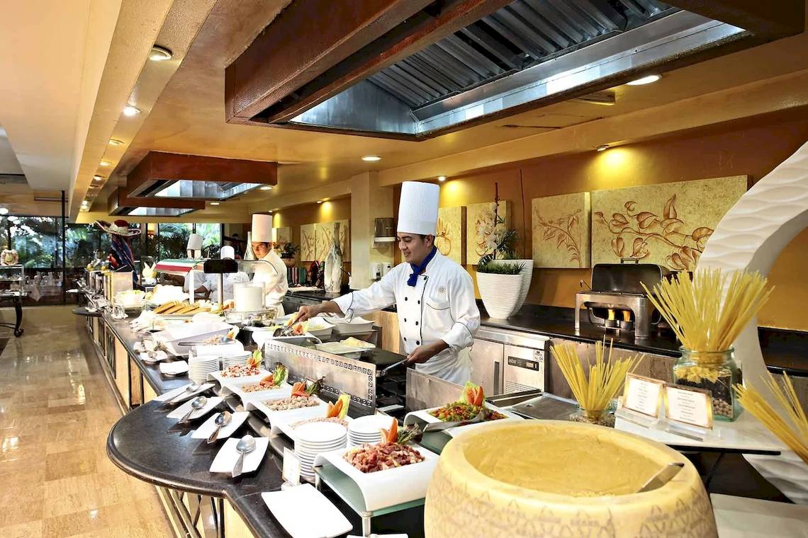 Buffet-Tisch im Hotel Bahia Principe Luxury Akumal mit verschiedenen Speisen und Köchen, die Gerichte zubereiten.