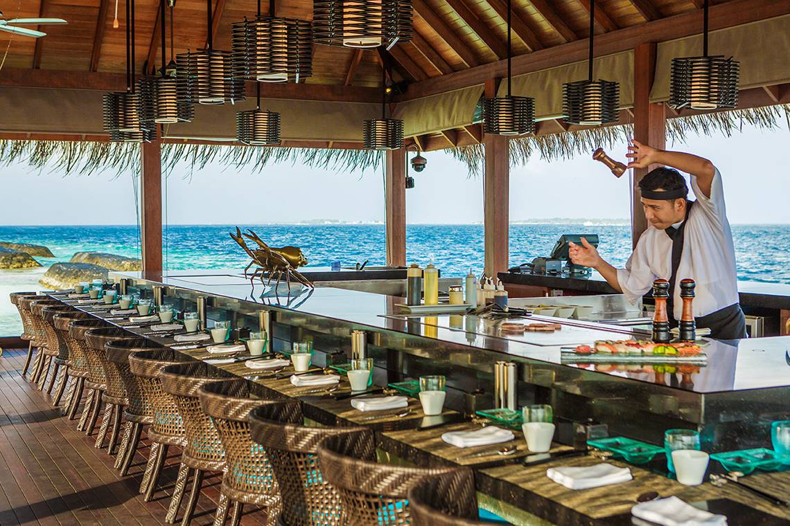 Ein Sushi-Bar im Kurumba Maldives mit Blick auf das Meer und einem Mann, der eine Zutat würzt.