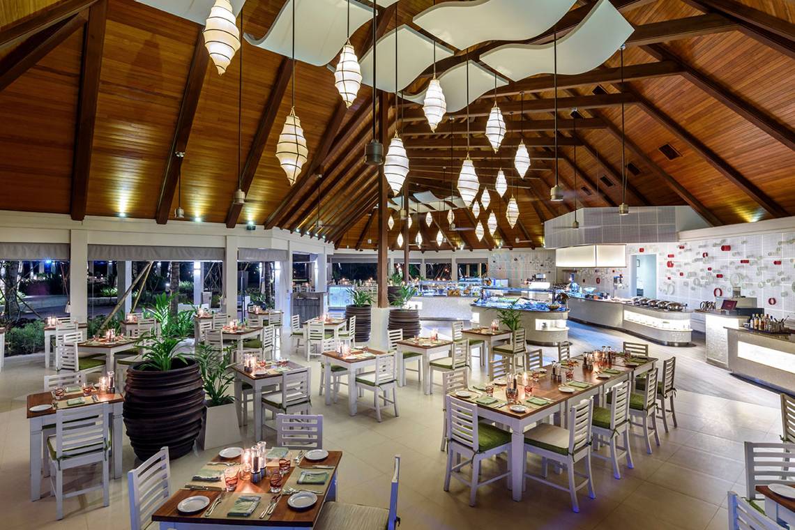 Innenbereich des Kurumba Maldives Hotels mit Restaurantbereich, Tischen und Stühlen.