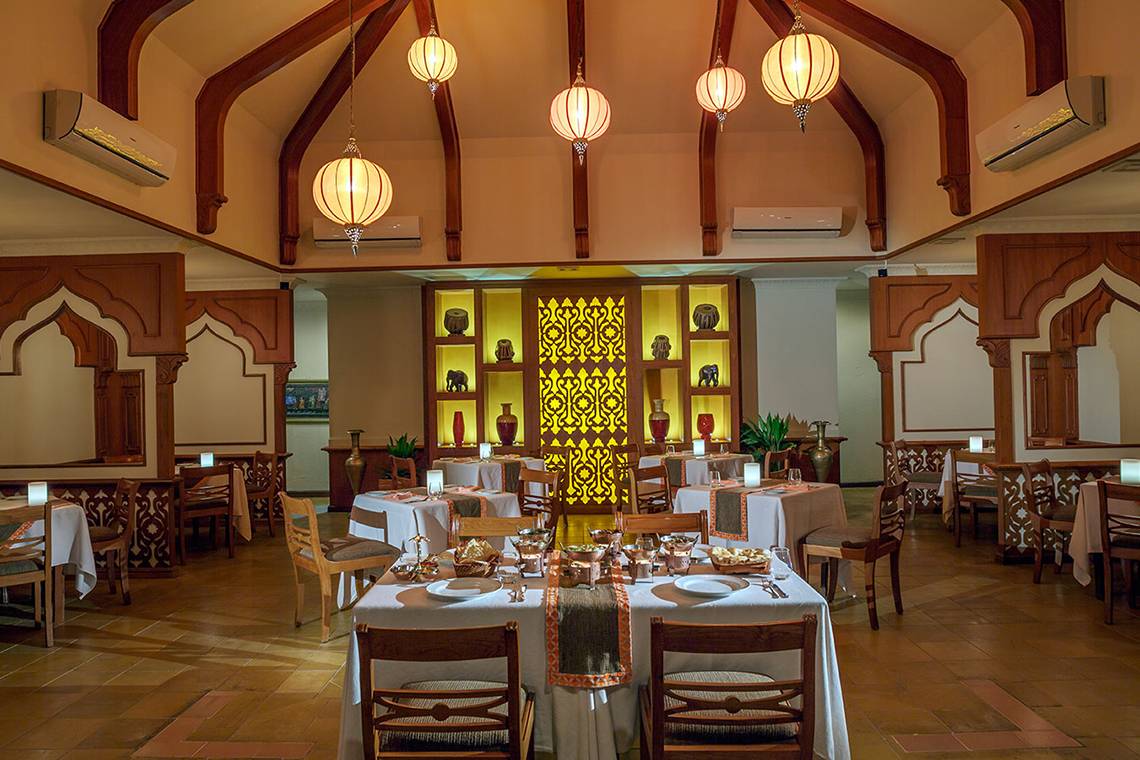 Innenbereich des Restaurants im Kurumba Maldives mit gedeckten Tischen, Holzmöbeln und traditionellen Lampen.