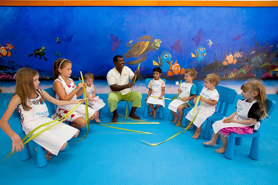 Ein Kurs im Kurumba Maldives mit Kindern und einem Lehrer vor einem blauen Wandbild mit Meerestieren.