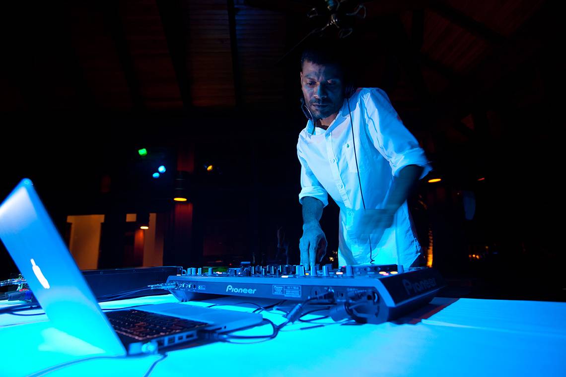 Ein DJ spielt Musik im Kurumba Maldives bei Nacht, mit Laptop und Mixer auf dem Tisch.