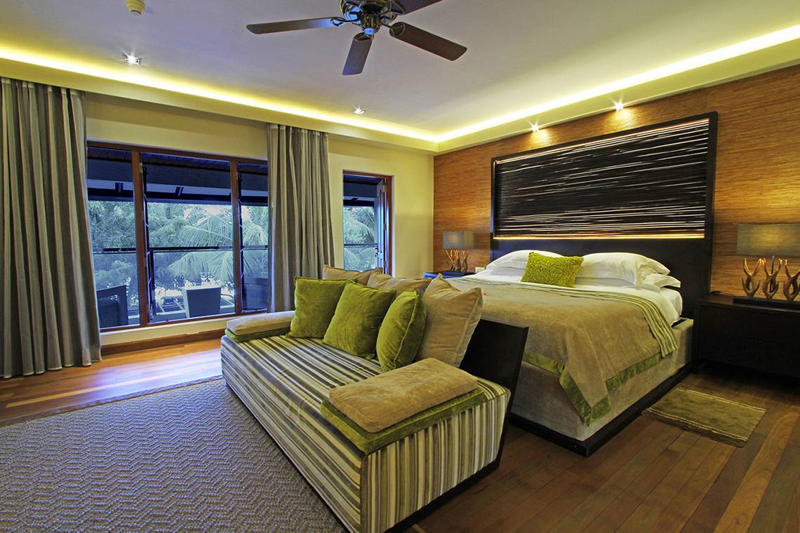 Schlafzimmer im Kurumba Maldives Hotel mit großem Bett, Fenstern und Holzboden.