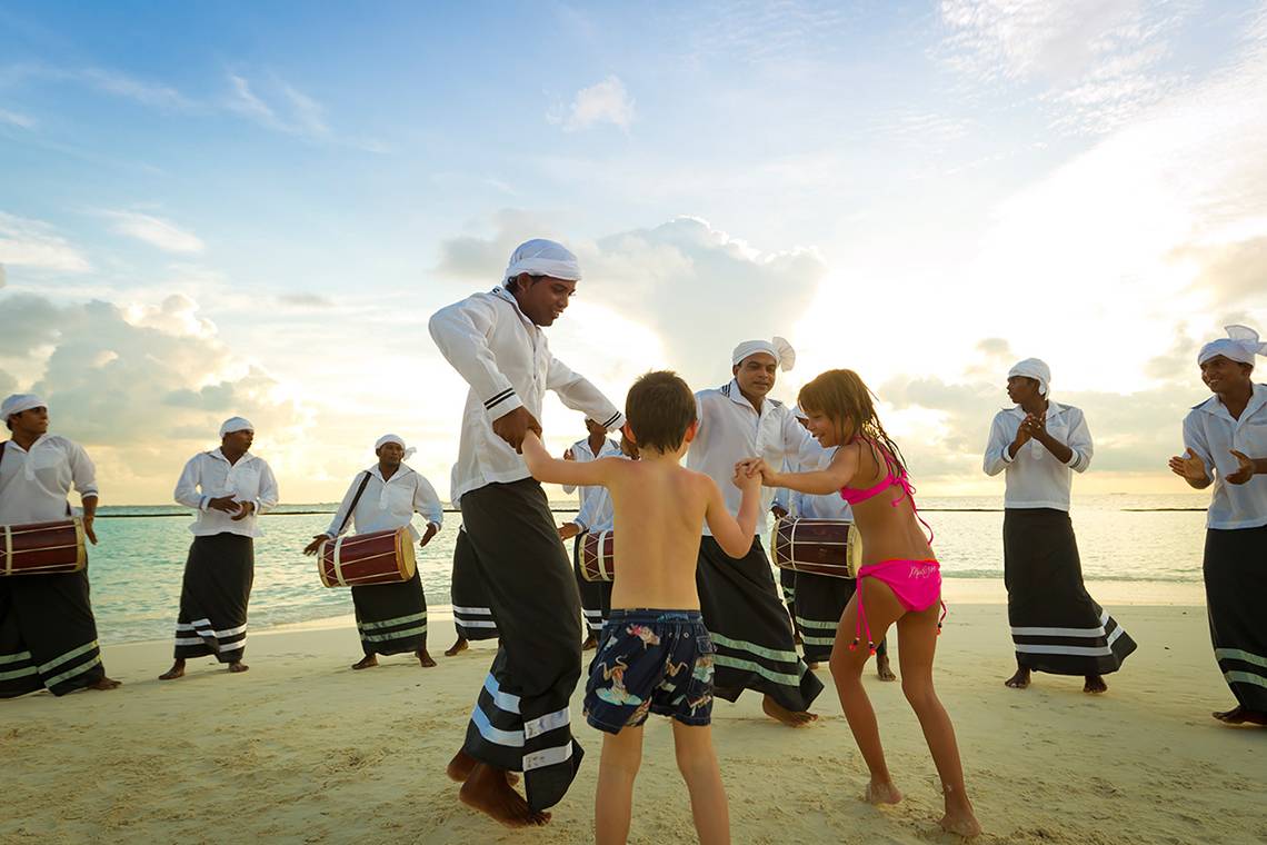 Eine Tanzgruppe am Strand des Kurumba Maldives Hotels mit einem kleinen Jungen und Mädchen.