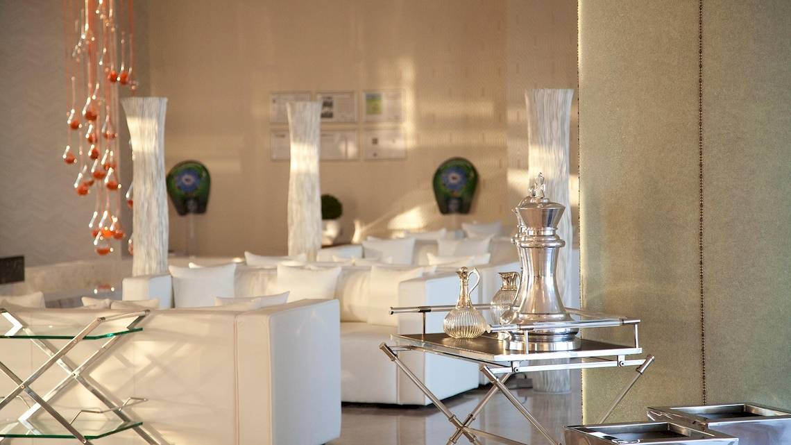 Hotellobby des Sentido Port Royal Villas & Spa mit weißen Möbeln und Silbergegenständen.