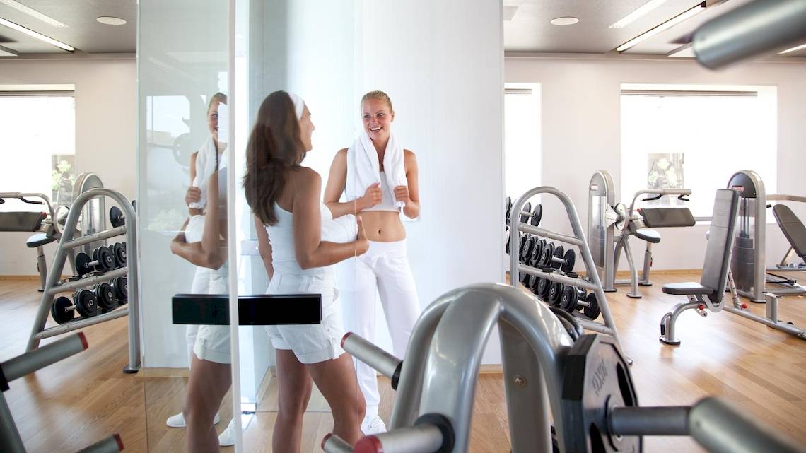 Fitnessstudio im Sentido Port Royal Villas & Spa mit zwei Frauen, die sich gegenseitig anfeuern.