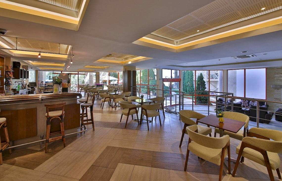 Innenbereich der Bar im Kaliakra Beach Hotel mit Holzboden, Tischen, Stühlen und einer Theke.