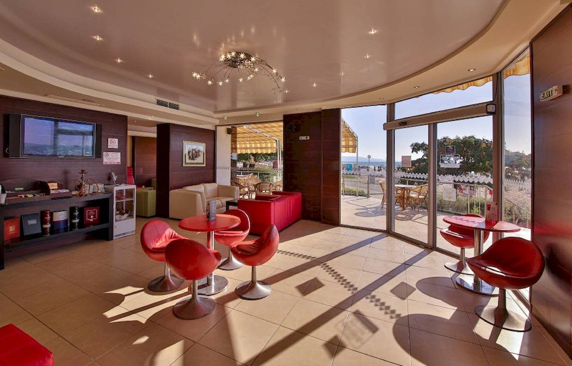 Loungebereich des Kaliakra Beach Hotels mit roten Stühlen und Tischen, Fernseher und Panoramafenstern