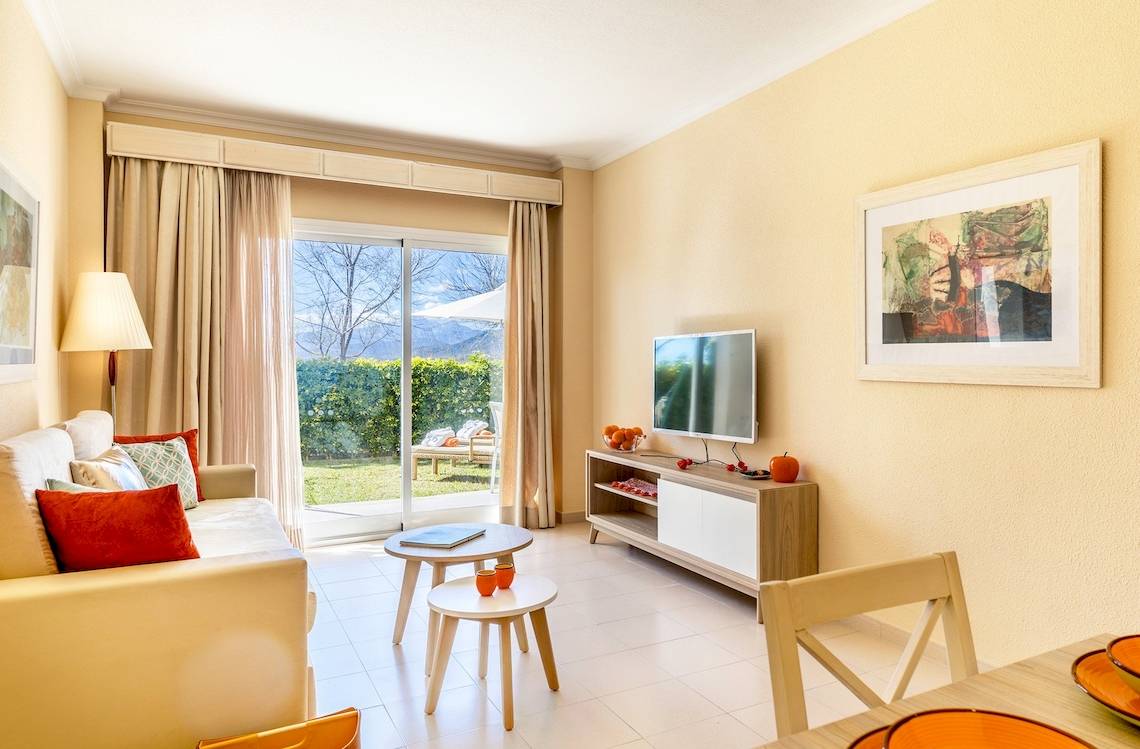 Wohnzimmer im VIVA Blue & Spa Hotel mit Couch, Tisch, Fernseher und Glastür zum Garten.